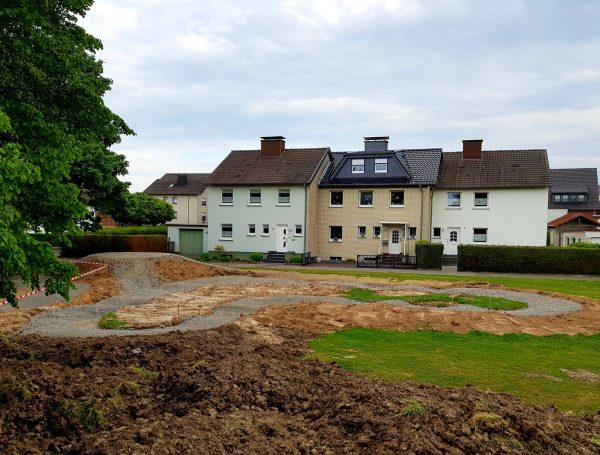 23.05.2022: Blick vom Sonnenhügel, wo später das Waldsofa steht, auf die Mountainbikestrecke im Schatten der Bäume, auf die Asphaltbahn und die Boulebahn. Im Vordergrund der neue Sitzplatz für die Boulespieler. Jetzt ist bis Pfingsten leider Baustopp, wegen Lieferverzögerung der Fertigteile für die Spieltunnel.