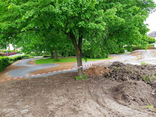 23.05.2022: Blick vom Sonnenhügel, wo später das Waldsofa steht, auf die Mountainbikestrecke im Schatten der Bäume, auf die Asphaltbahn und die Boulebahn. Im Vordergrund der neue Sitzplatz für die Boulespieler. Jetzt ist bis Pfingsten leider Baustopp, wegen Lieferverzögerung der Fertigteile für die Spieltunnel.